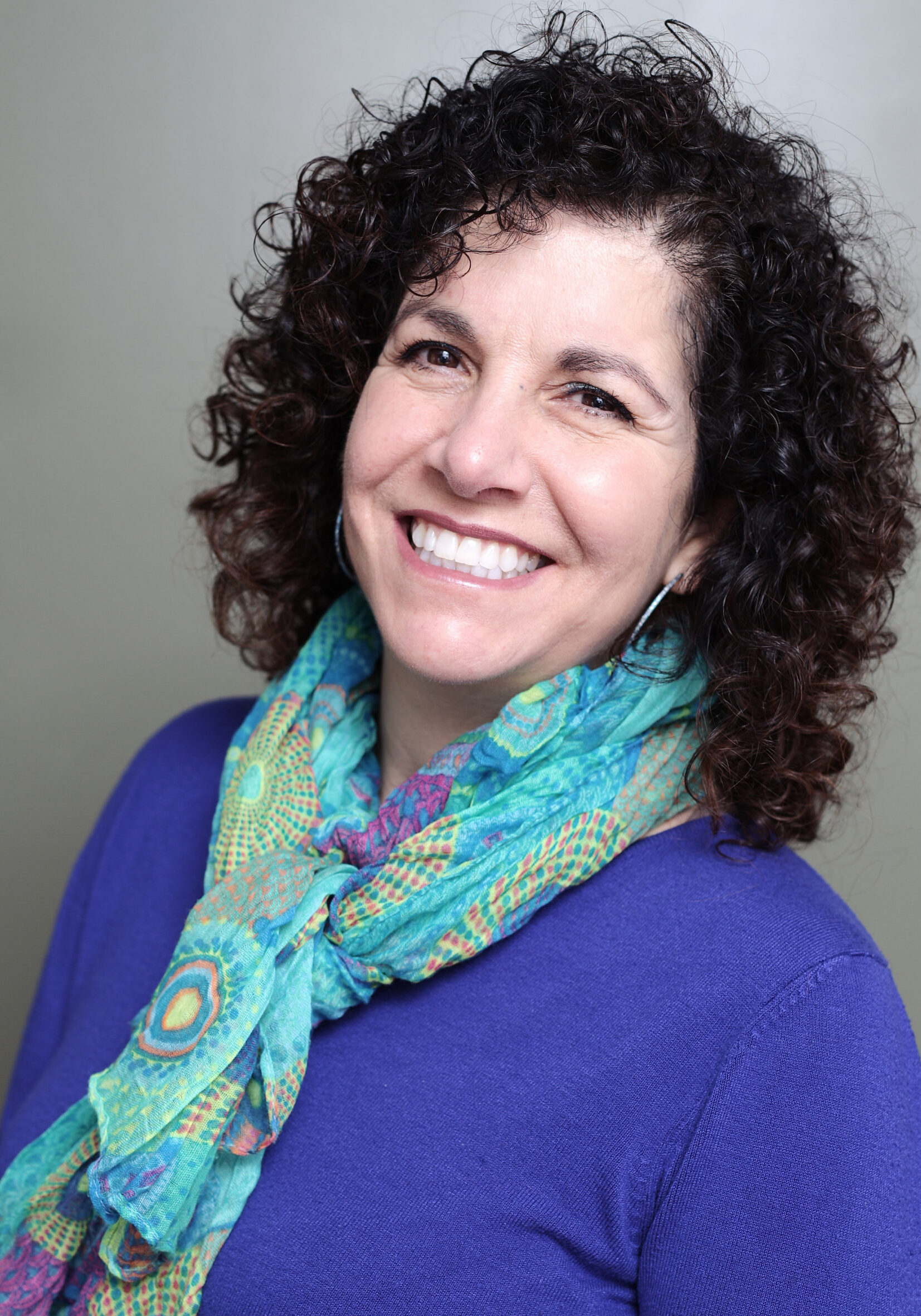 A woman with curly hair wearing a blue shirt and a scarf.